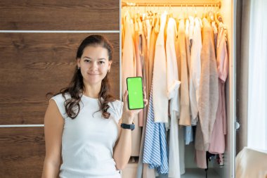 Uygulamada eski istenmeyen kıyafetleri satmak için akıllı telefon uygulaması kullanan genç bir kadın. Krom yeşil ekran. Yüksek kalite fotoğraf