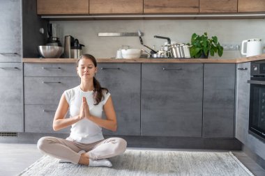 Genç bir kadın mutfakta oturmuş kirli bulaşıkların arka planı üzerine meditasyon yapıyor. Yavaşla, kendine dikkat et, yavaş yaşam konsepti. Yüksek kalite fotoğraf