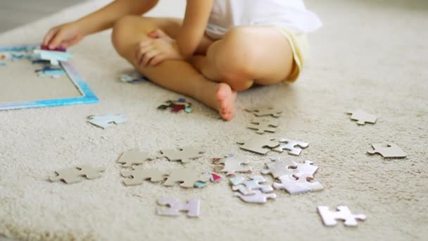 小さな金髪の女の子はカーペットの上に家に座ってパズルを収集します パズルのピースに集中する 高品質の4K映像 — ストック動画