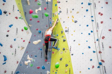Prag spor merkezinin içindeki yapay duvara tırmanan renkli kancalara asılı kaya tırmanışçısı genç bir kadın. Ekstrem spor ve kaya konsepti. Yüksek kalite fotoğraf