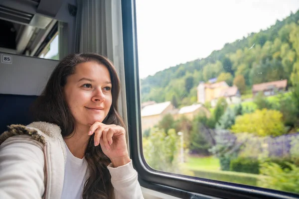 Young woman looking through the train window. Happy train passenger traveling and looking through the window, Europe. High quality photo