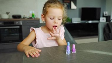 Küçük kız evde manikür yapıyor ve renkli pembe, mavi ve mor ojeli tırnaklar boyuyor. Ojeyi kurutmak için tırnaklarını üfleyen kız çocuğu. Yüksek kalite 4k görüntü