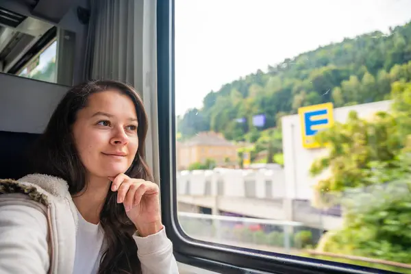 Young woman looking through the train window. Happy train passenger traveling and looking through the window. High quality photo