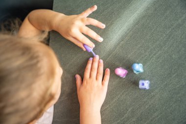 Küçük kızın manikür yaptığı ve evde pembe, mavi ve mor ojeli oje sürdüğü en iyi manzara. Yüksek kalite fotoğraf