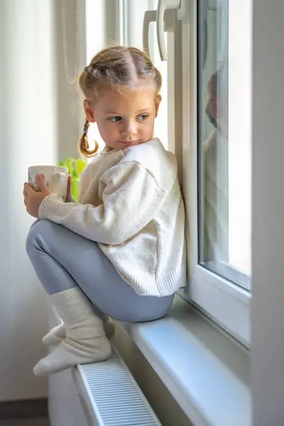 Petite Fille Mignonne Pull Chaud Chaussettes Assis Regardant Par Fenêtre Image En Vente