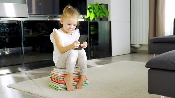 Linda Niña Sienta Una Pila Libros Para Niños Utiliza Teléfono — Vídeos de Stock