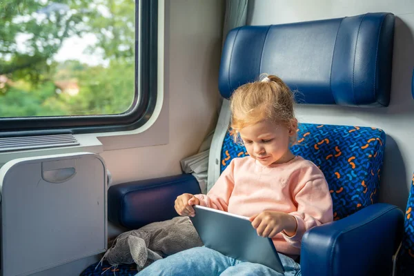 Beautiful Little girl using digital tablet during traveling by railway, Europe. High quality photo