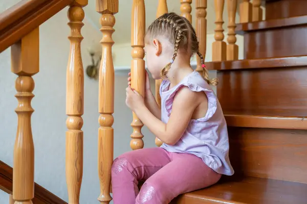Little girl is sitting on stairs at home. Dangerous situation at home. Child safety concept. High quality photo