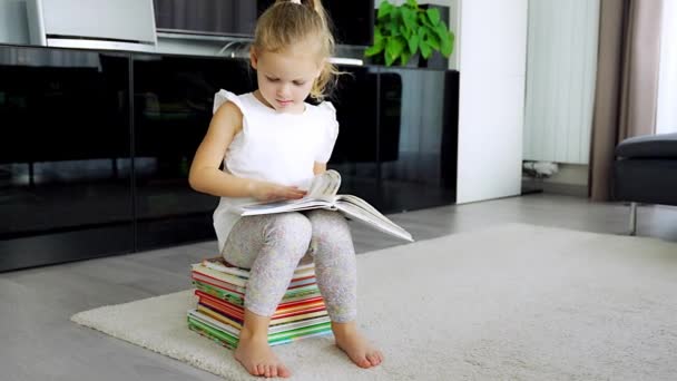 Κοριτσάκι Κάθεται Πάνω Ένα Σωρό Παιδικά Βιβλία Και Ξεφυλλίζει Ένα — Αρχείο Βίντεο
