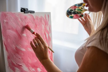 Paletli ve fırçalı genç kadın ressamın evdeki tuvale soyut pembe resim çizmesini yakından çek. Sanat ve yaratıcılık kavramı. Yüksek kalite fotoğraf