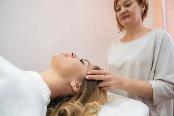 Healer performing by lightly touched set of 32 points of access bars on young woman head, stimulating positive change thoughts and emotions in salon. Alternative medicine concept. High quality photo