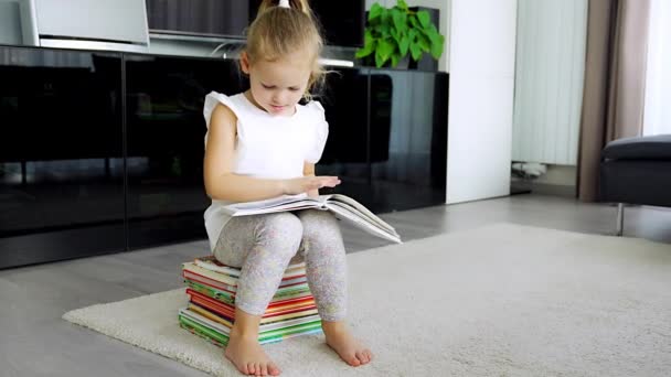 Klein Meisje Zit Een Stapel Kinderboeken Bladert Door Een Boek — Stockvideo