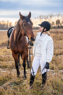 Güzel sarışın, profesyonel bayan jokey kışın atın yanında duruyor. At konseptiyle arkadaşlık. Yüksek kalite fotoğraf