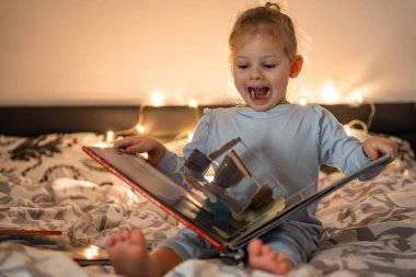 Noel ortamında evde kitap okuyan ve ışık alan küçük bir kız. Yüksek kalite fotoğraf