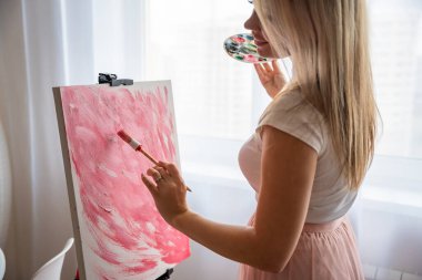 Paletli ve fırçalı genç sarışın kadın ressam evdeki tuvale soyut pembe resim çiziyor. Sanat ve yaratıcılık kavramı. Yüksek kalite fotoğraf