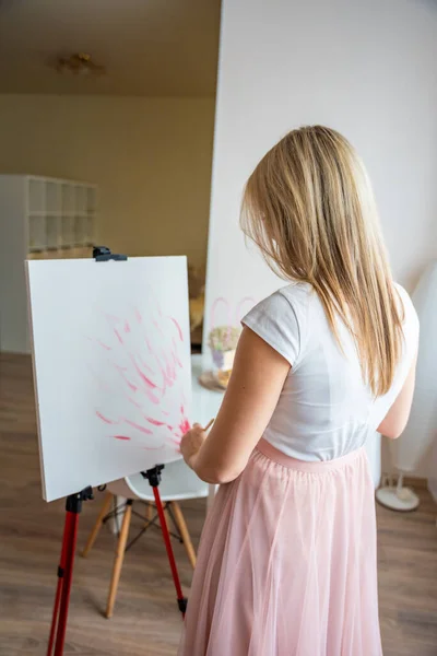 Young woman artist with palette and brush starts to paint abstract pink picture on canvas at home. Art and creativity concept. High quality photo