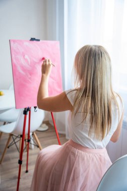 Paletli ve fırçalı genç sarışın kadın ressam evdeki pencerenin yanındaki tuvale soyut pembe resim çiziyor. Sanat ve yaratıcılık kavramı. Yüksek kalite fotoğraf