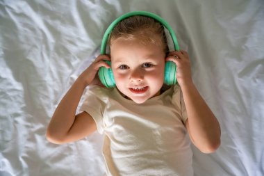 Evde yatağında kulaklık takıp müzik dinleyen şirin küçük kız. Yüksek kalite fotoğraf