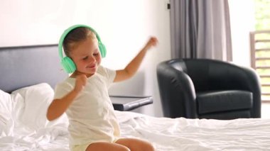 Çocuk kulaklıklarıyla müzik dinleyen ve mutlu bir sabahta evde dans eden küçük bir kızın portresi. Yüksek kalite 4k görüntü