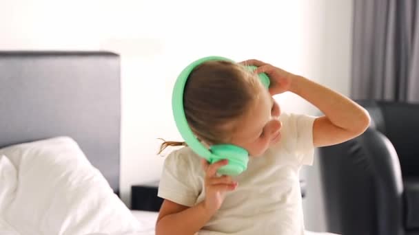 家庭のベッドで緑の子供のヘッドフォンを使用して音楽を楽しむ小さな女の子 高品質の4K映像 — ストック動画