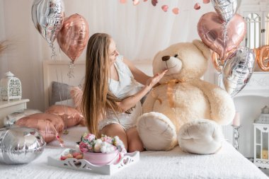 Beautiful young girl at home on the bed in the morning enjoy valentines day celebration with heart shaped balloons. High quality photo