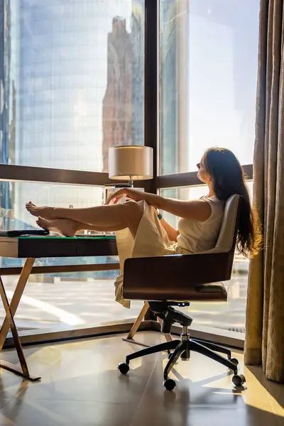 Stylish businesswoman freelancer working with laptop and laying on the chair, enjoying panoramic view in the city background. Low key photo. High quality photo