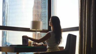 Stylish businesswoman freelancer stops working with laptop and stretches, she is sitting on the chair, enjoying panoramic view in the city background. Low key video. High quality 4k footage