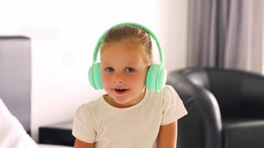 Portrait of little girl singing and listening music with green kids headphones in home bedroom. High quality 4k footage