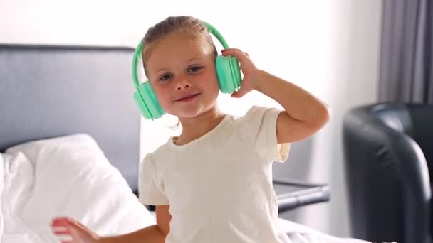 家のベッドで緑色の子供のヘッドフォンで音楽を聞いている少女の肖像画 高品質の4K映像 — ストック動画