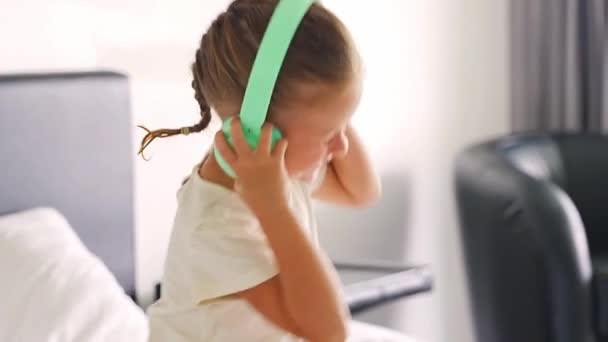 笑顔の小さな少女は緑の子供のヘッドフォンを使用して音楽を楽しんでいます 高品質の4K映像 — ストック動画