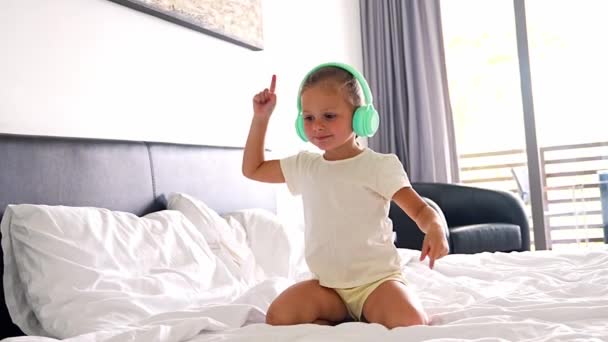 子供のヘッドフォンで音楽を楽しんで 自宅でベッドで踊っている小さな女の子 高品質の4K映像 — ストック動画