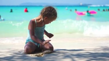 Denizdeki kumda oynayan küçük bir kız, deniz beyazının arka planı ve mavi su. Tatil ve çocuk konseptiyle seyahat. Yüksek kalite 4k görüntü