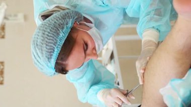 Dermatolog cerrahın portresi ameliyattan sonra yarayı dikiyor, ameliyat sürecine yakından bakıyor. Dikey video. Yüksek kalite 4k görüntü