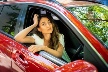 Happy smiling woman driver behind the wheel red car. View through car window. High quality photo