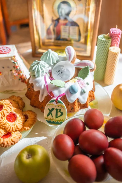 Easter cake with painted eggs, apples and cookies on table in home kitchen. Church icons and candle on background. Orthodox religion theme. High quality photo