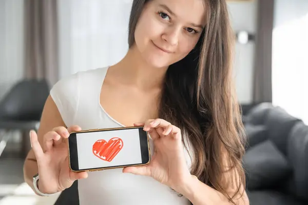 World Health Day concept. Young woman showing illustration of heart on her smartphone, illustrating the importance of cardiovascular health awareness on international health observation.