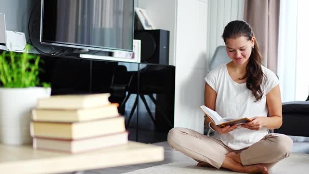 Χαμογελώντας Νεαρή Γυναίκα Διαβάζει Βιβλίο Κάθεται Στο Πάτωμα Στο Σαλόνι — Αρχείο Βίντεο