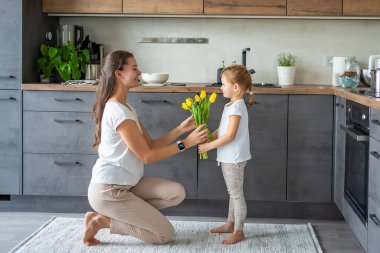 Küçük kız mutfakta annesine sarı laleler veriyor. Anneler günü, doğum günü ya da 8. Uluslararası Kadınlar Günü konsepti. Yüksek kalite fotoğraf