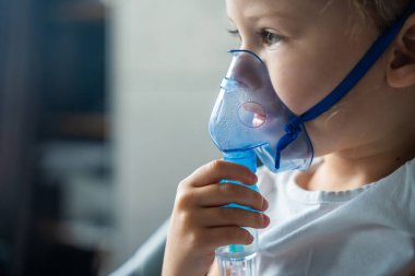 Küçük kızın yakın plan görüntüsü nebulizör maskesini tutuyor ve yüzüne yaslanıyor, solunum yolu tedavisi kavramı. Yüksek kalite fotoğraf