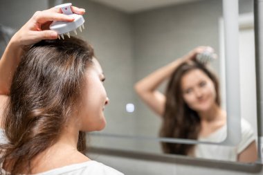 Saç masajı yapan genç bir kadın. Kafa masajı yapan bir kadın. Evde saç uzatmak için saç fırçası kullanan bir kadın. Aynanın yansıyan görüntüsü. Yüksek kalite fotoğraf