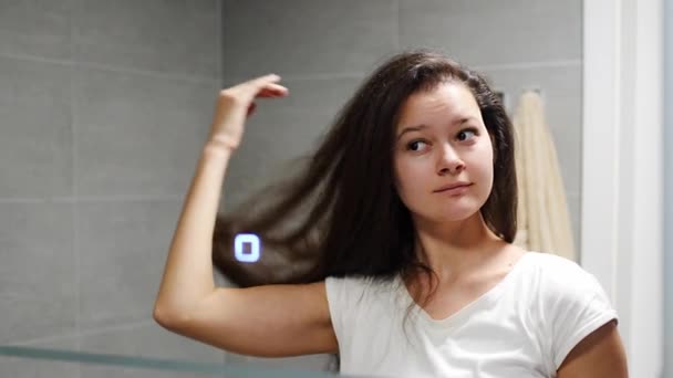 Jovem Mulher Olha Para Espelho Banheiro Toca Seu Cabelo Escuro — Vídeo de Stock