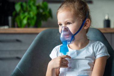Şirin küçük kız oturuyor ve elinde nebulizör maskesiyle yüzüne yaslanıyor, hava yolu tedavisi kavramı. Yüksek kalite fotoğraf