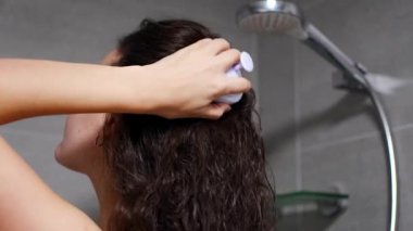 Koyu kıvırcık saçlı genç bir kadın kafa derisi masajı yapıyor ya da saç büyümesi için saç fırçasıyla ev banyosunda masaj yapıyor. Yüksek kalite 4k görüntü