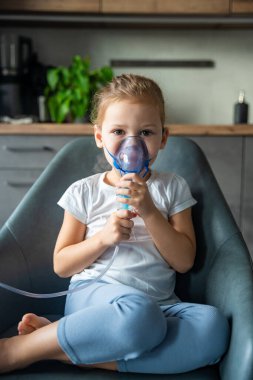 Şirin küçük kız elinde nebulizör maskesiyle oturmuş hastalık izninde yüzüne yaslanıyor, hava yolu tedavisi kavramı. Yüksek kalite fotoğraf