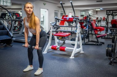 Genç bir kadın elinde dambıllarla spor salonunda egzersiz yapıyor. Yüksek kalite fotoğraf