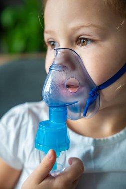 Küçük kızın yakın plan görüntüsü nebulizör maskesini tutuyor ve yüzüne yaslanıyor, solunum yolu tedavisi kavramı. Yüksek kalite fotoğraf