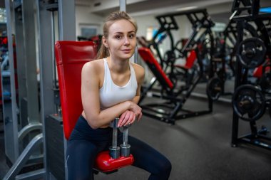 Elinde dambıllarla poz veren ve spor salonunda egzersiz yapan genç bir kadın. Yüksek kalite fotoğraf