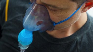 Evde nebulizör maskesi takan sağlıksız bir adam nefes alıyor. Sağlık, tıbbi ekipman ve insan konsepti. Yüksek kalite 4k görüntü