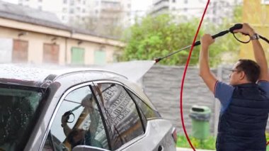 Genç bir adam arabasını tazyikli su ve köpüklü bir hortumla oto yıkamada yıkıyor. Yüksek kalite 4k görüntü