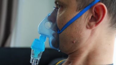 Evde nebulizör maskesi takan sağlıksız bir adam nefes alıyor. Sağlık, tıbbi ekipman ve insan konsepti. Yüksek kalite 4k görüntü